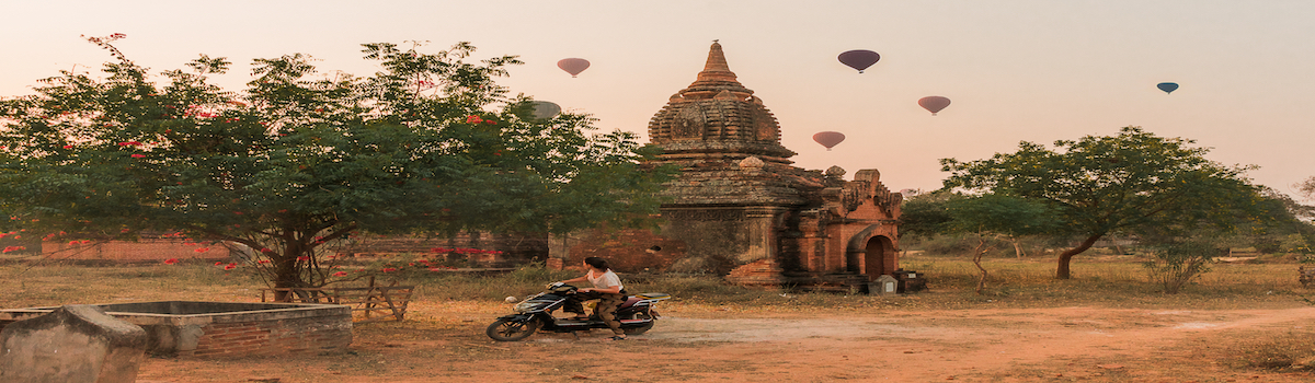 Woman riding a bike looking baloons over the temples at sunrise in Bagan, Myanmar, Balloon over Bagan and ebike riding woman